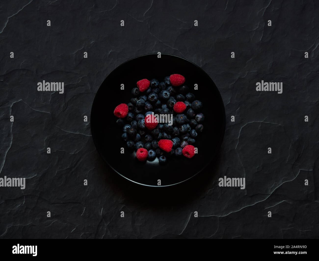 I mirtilli e lamponi in un piatto nero su una pietra scura sullo sfondo visto dal di sopra, flatlay concetto in studio. Foto Stock