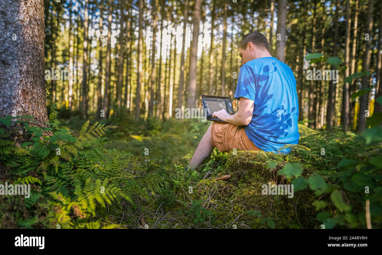 Un sano equilibrio tra lavoro e vita familiare - lavorare con un computer portatile in una foresta verde. Foto Stock