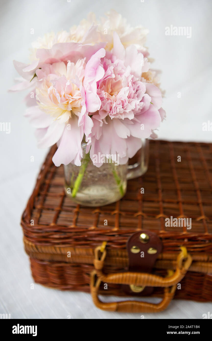 Un bellissimo mazzo di peonie rosa in un vaso sorge su una valigia di legno. Bella composizione. Foto Stock