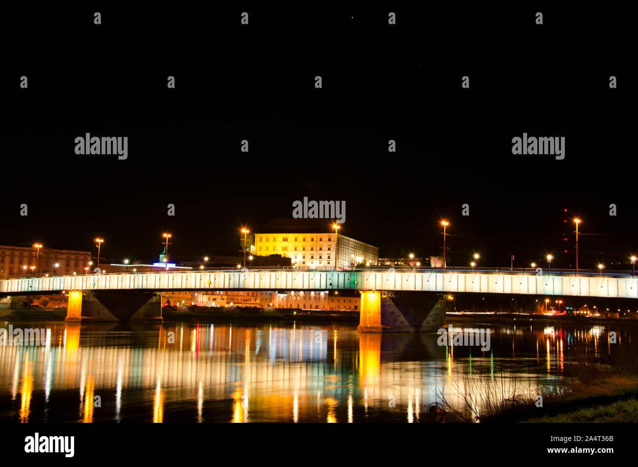 Bella ipnotiche scena notturna vista panoramica di Linz Nibelungen ponte sul fiume Danubio con golden luci colorate le riflessioni sulla superficie dell'acqua. Foto Stock