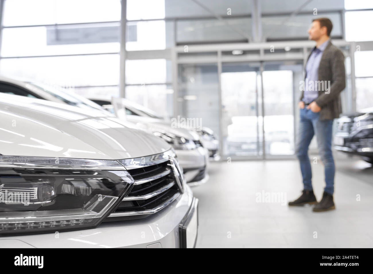 Messa a fuoco selettiva dei proiettori di grande bianco auto in auto salon. Giovane maschio cliente sta guardando le nuove auto e scegliendo in piedi a sfondo inn car showroom. Concetto di acquisto di automobile. Foto Stock