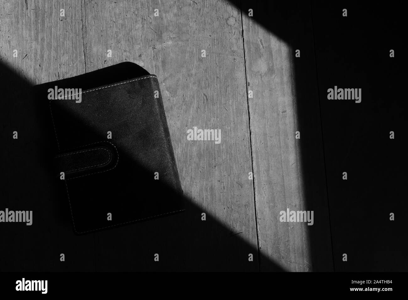 Un libro nero posto sulla superficie di legno sotto la luce del sole, immagine in bianco e nero Foto Stock