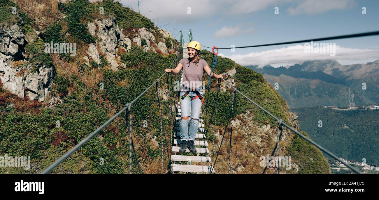 Extreme passeggiate femmina su un ponte di sospensione in montagna su un precipizio Foto Stock