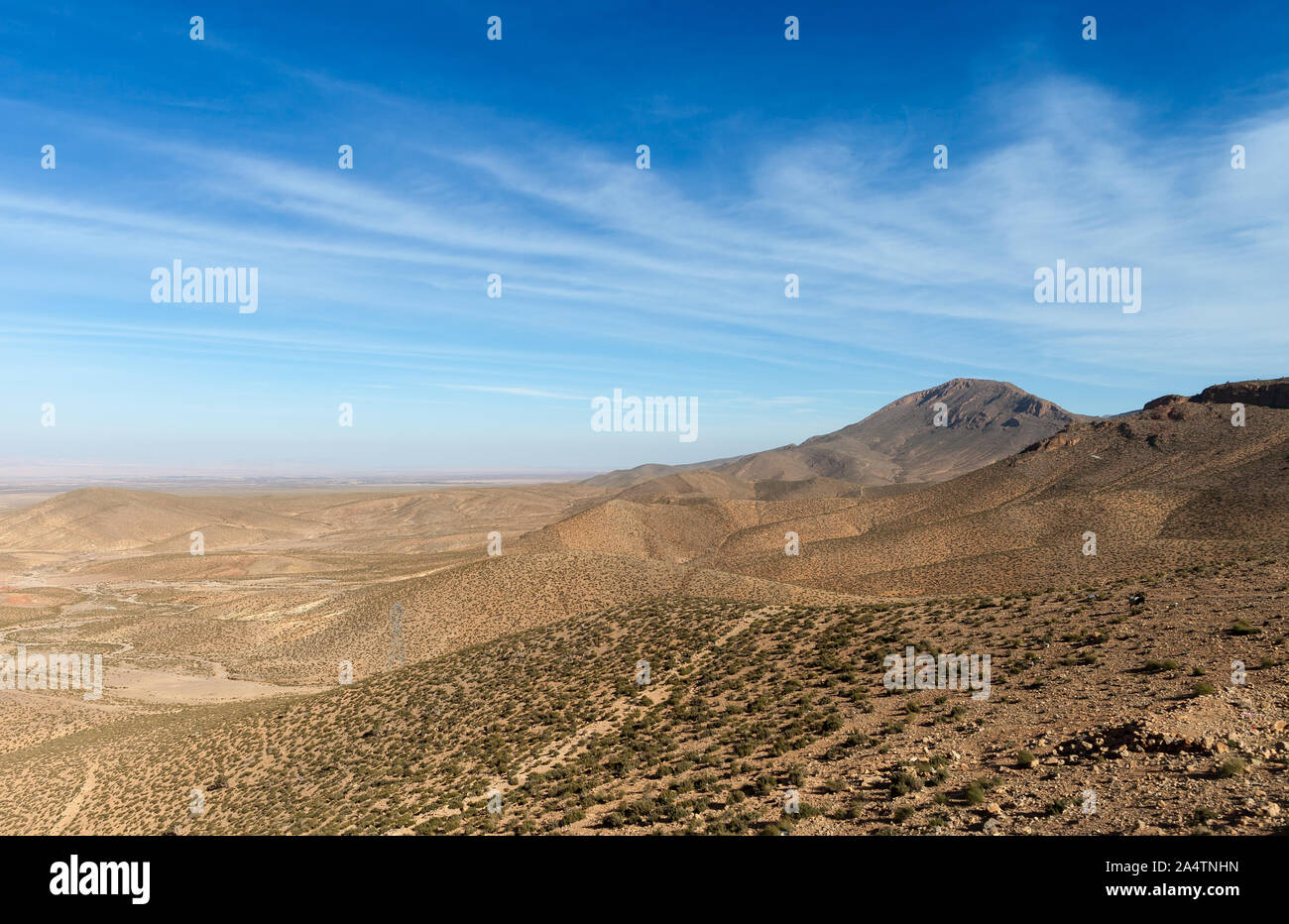 Affacciato su una gamma della montagna di Atlas Moutnain gamma in Marocco. Alcuni piccoli arbusti e alberi visti di fronte a un bel cielo azzurro coperto da alcune nuvole Foto Stock