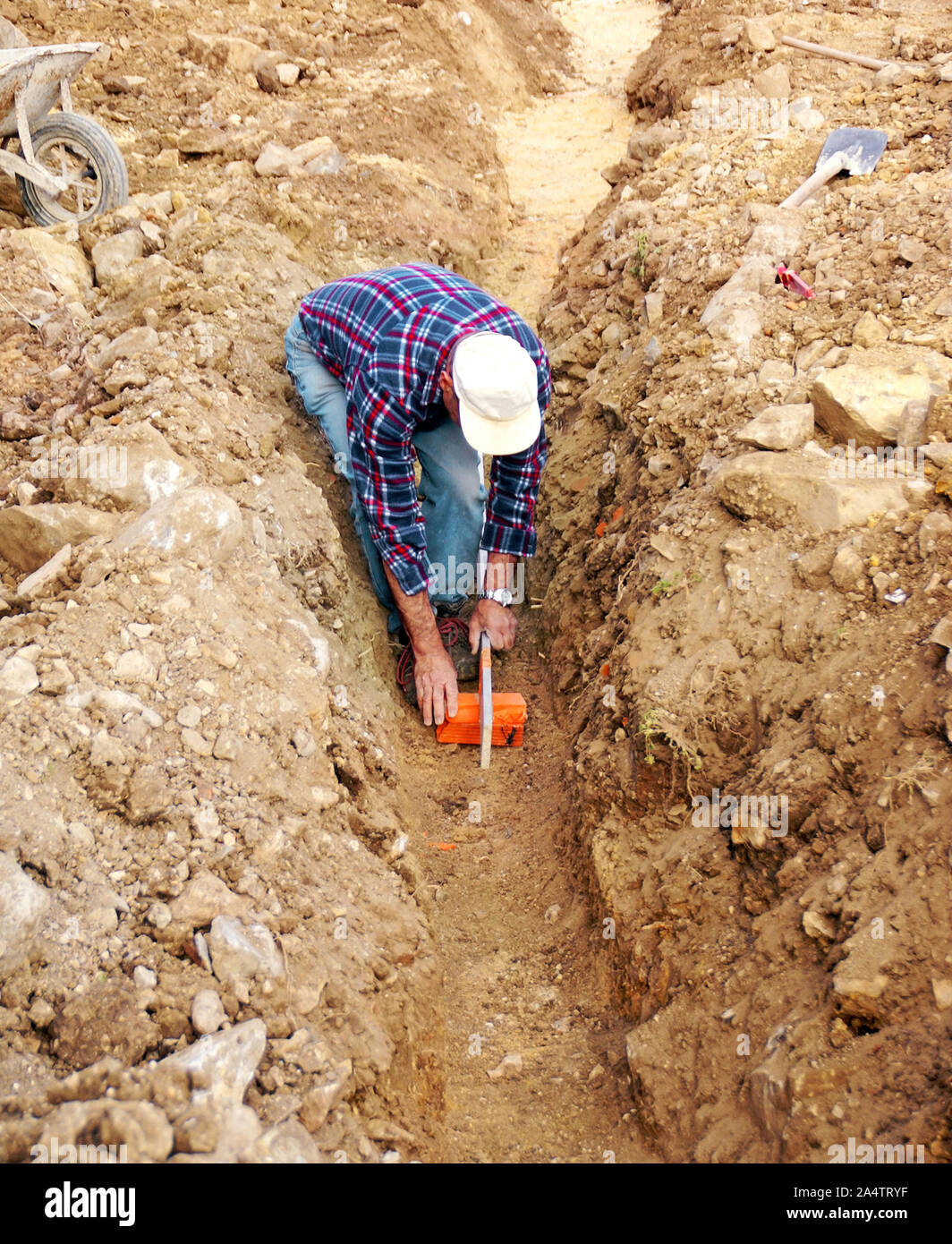 Verifica da parte di un lavoratore della pendenza di una trincea per la connessione di una casa per la rete pubblica. Foto Stock