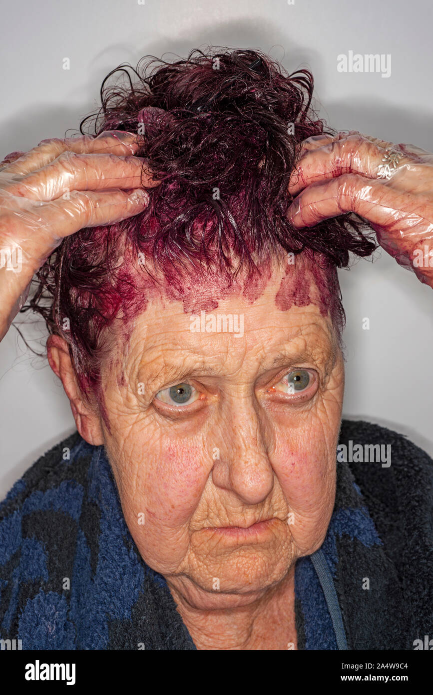 Donna anziana tingere i capelli a casa Foto Stock