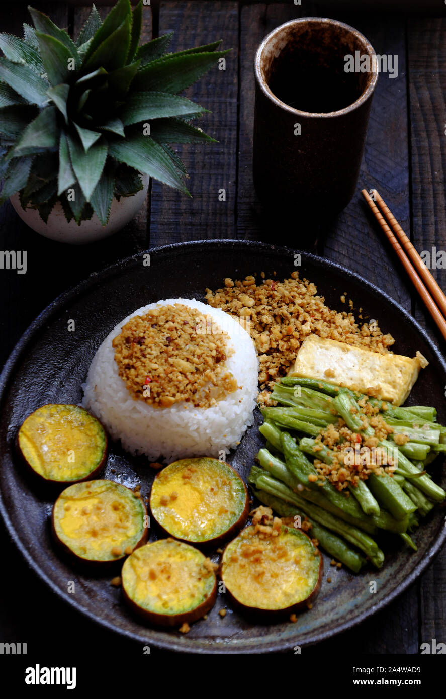 Vista da sopra la piastra nera del piatto di riso per pranzo un pasto vegano vietnamita in casa, mangiando cibo vegetariano con tofu, verdure grigliate, cowpea, nutrizione, Foto Stock