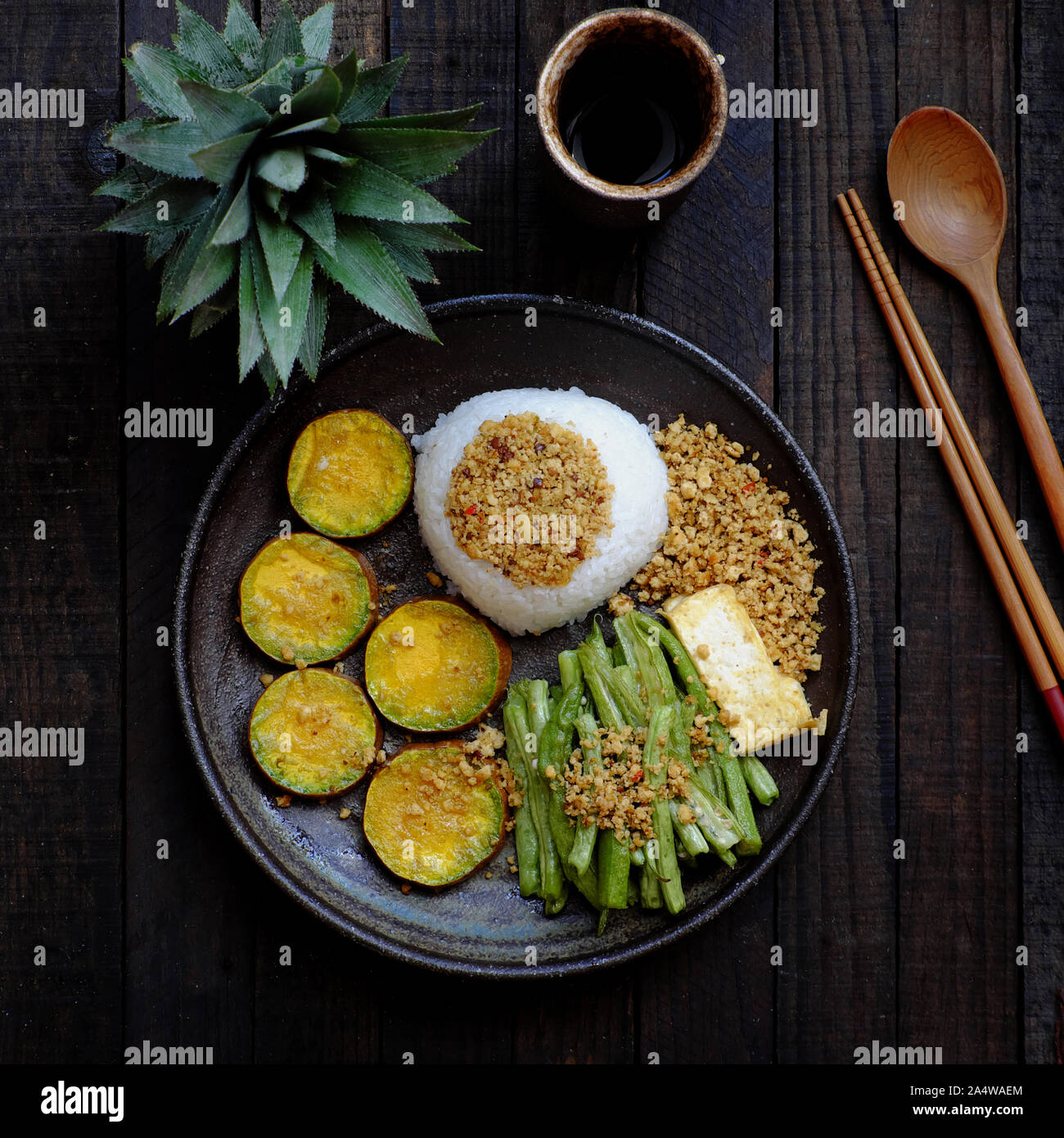 Vista da sopra la piastra nera del piatto di riso per pranzo un pasto vegano vietnamita in casa, mangiando cibo vegetariano con tofu, verdure grigliate, cowpea, nutrizione, Foto Stock