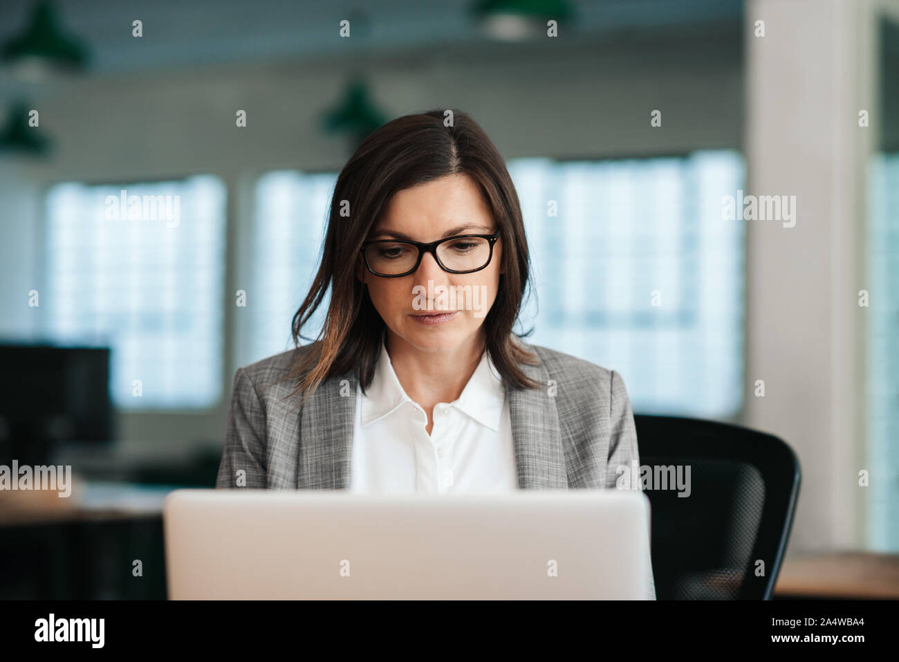 Focalizzato imprenditrice seduto alla sua scrivania che lavora su un notebook Foto Stock