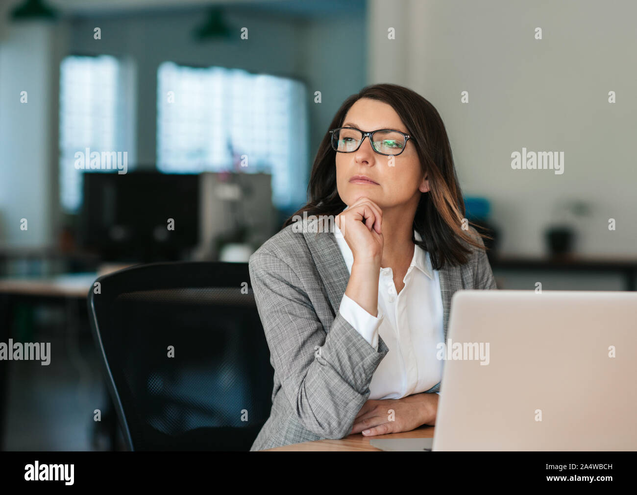 Imprenditrice pensando di lavorare mentre si è seduta alla sua scrivania in ufficio Foto Stock