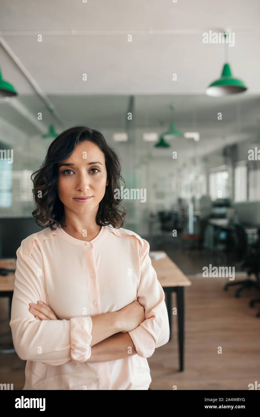 Imprenditrice sorridente in piedi con le braccia incrociate in un ufficio Foto Stock
