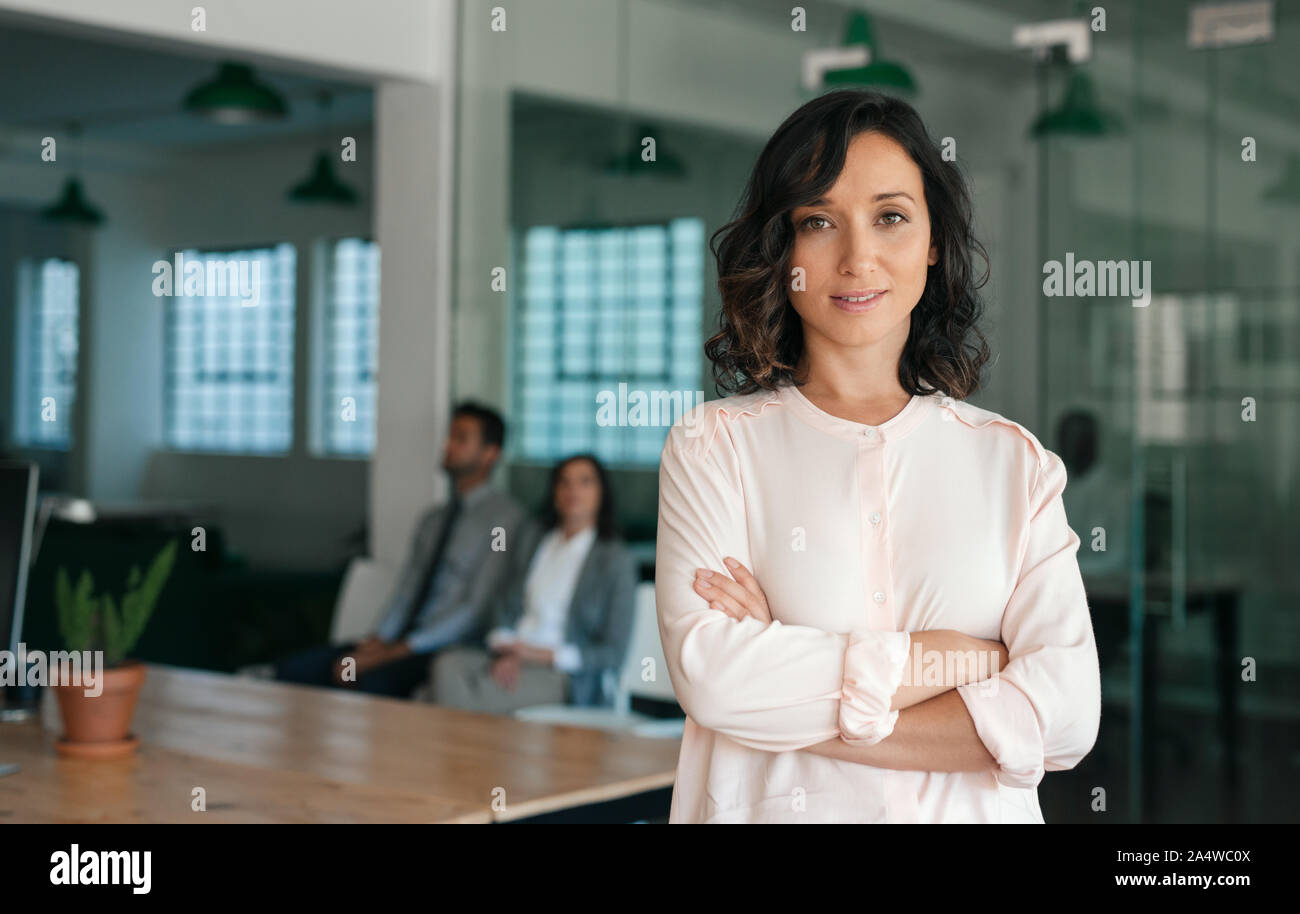 Sorridente giovane imprenditrice in piedi con fiducia in un ufficio di grandi dimensioni Foto Stock