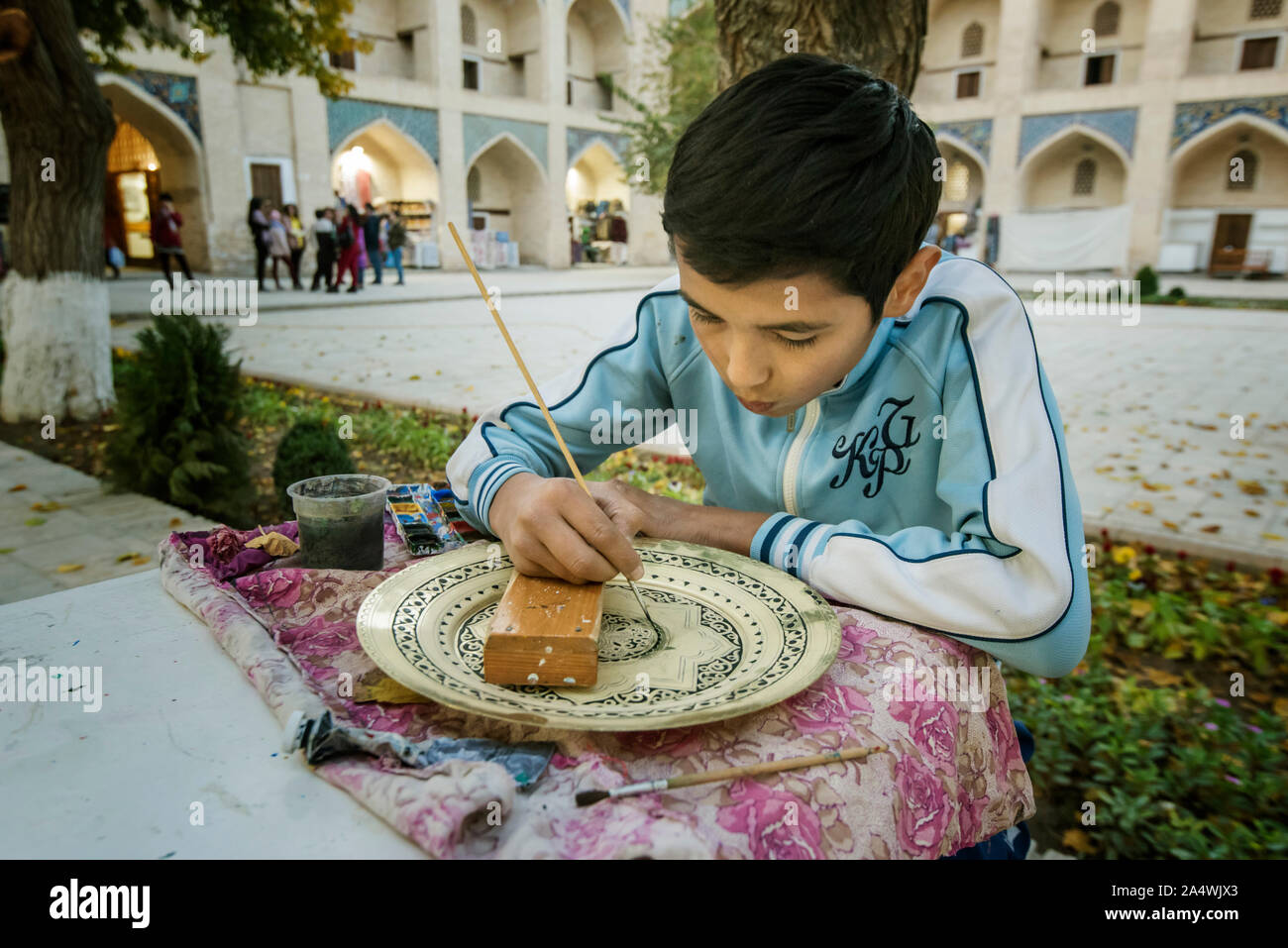 Un ragazzo dipinto una piastra. Nadir Divan Begi madrasa, oggi un centro per crafstmen. Bukhara, un sito Patrimonio Mondiale dell'UNESCO. Uzbekistan Foto Stock