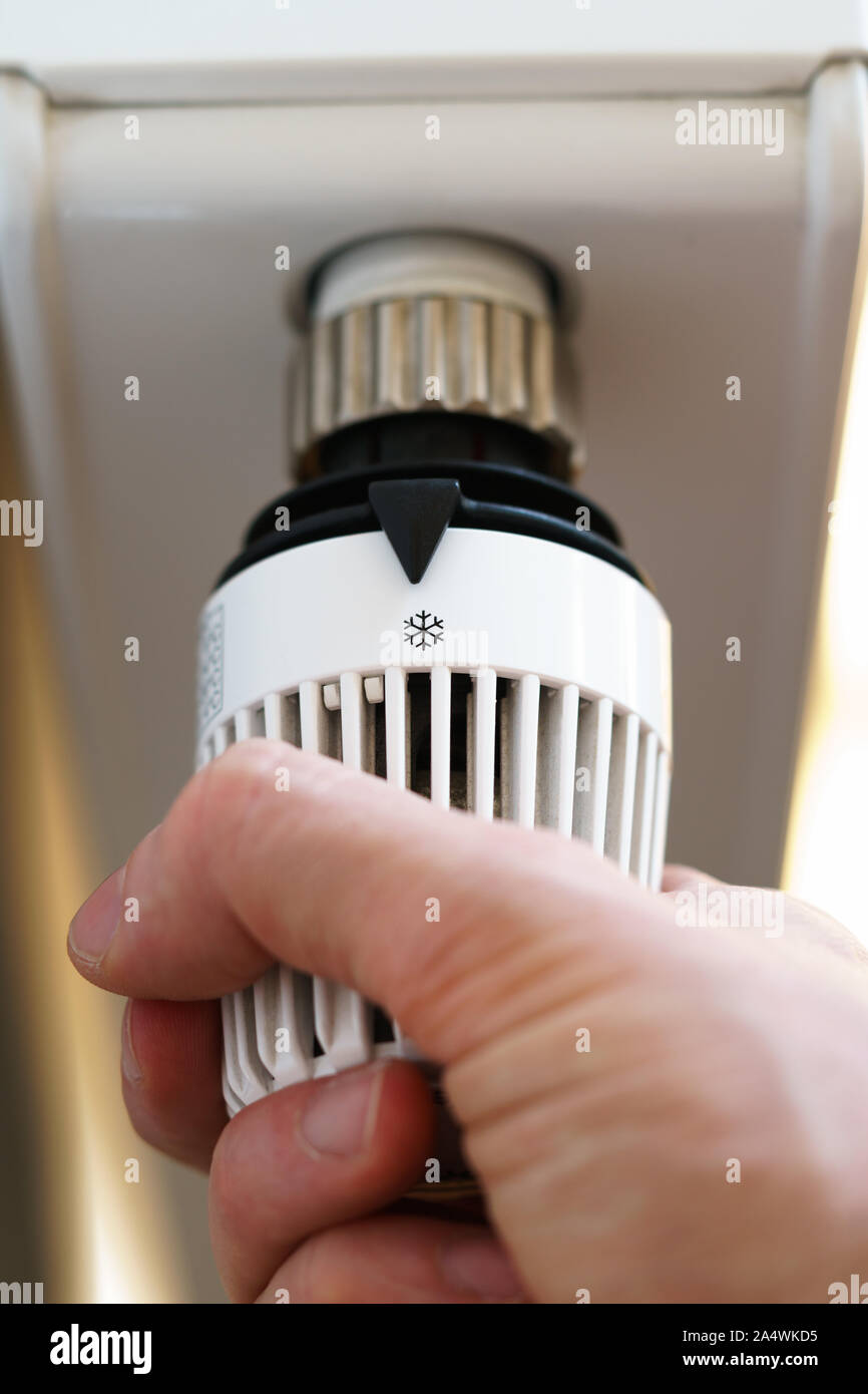 Mano di uomo regolazione valvola del termostato del radiatore a fiocco di neve icona di brina, simbolo per risparmiare soldi a spese di riscaldamento o a bassa temperatura, closeup, vertic Foto Stock