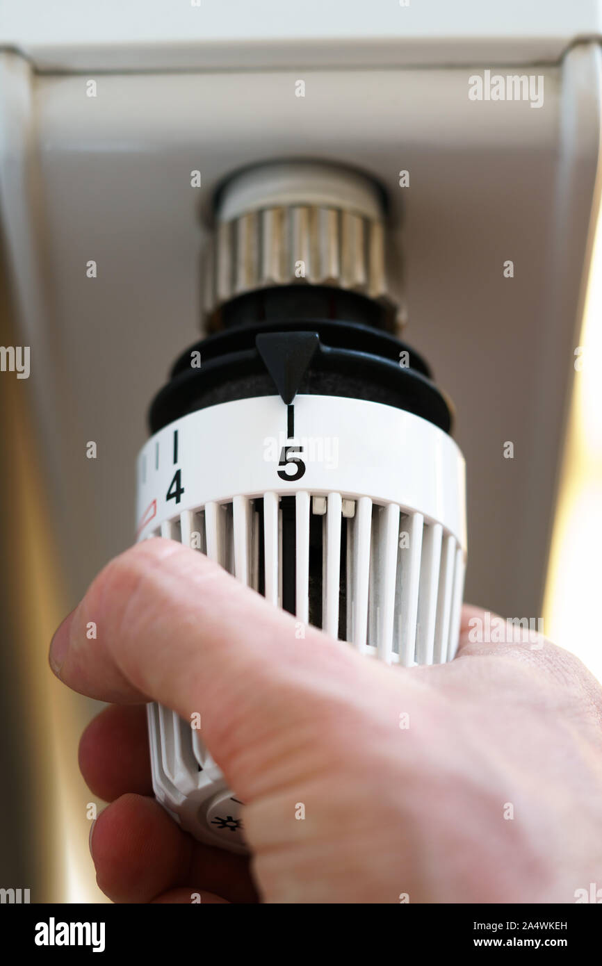 Mano di uomo regolazione valvola del termostato del radiatore fino al numero cinque icona, simbolo per alti costi di riscaldamento o la temperatura calda impostazione, closeup, verticale f Foto Stock