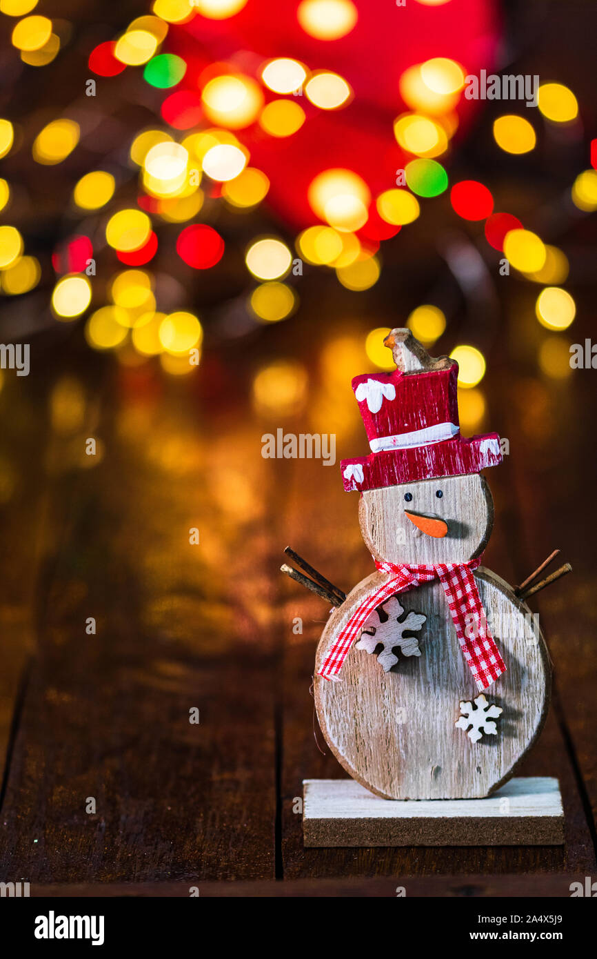 Le decorazioni di Natale contro sfondo sfocato e fuori fuoco luci. Legno decorativo pupazzo di neve e glittery palle di Natale Foto Stock