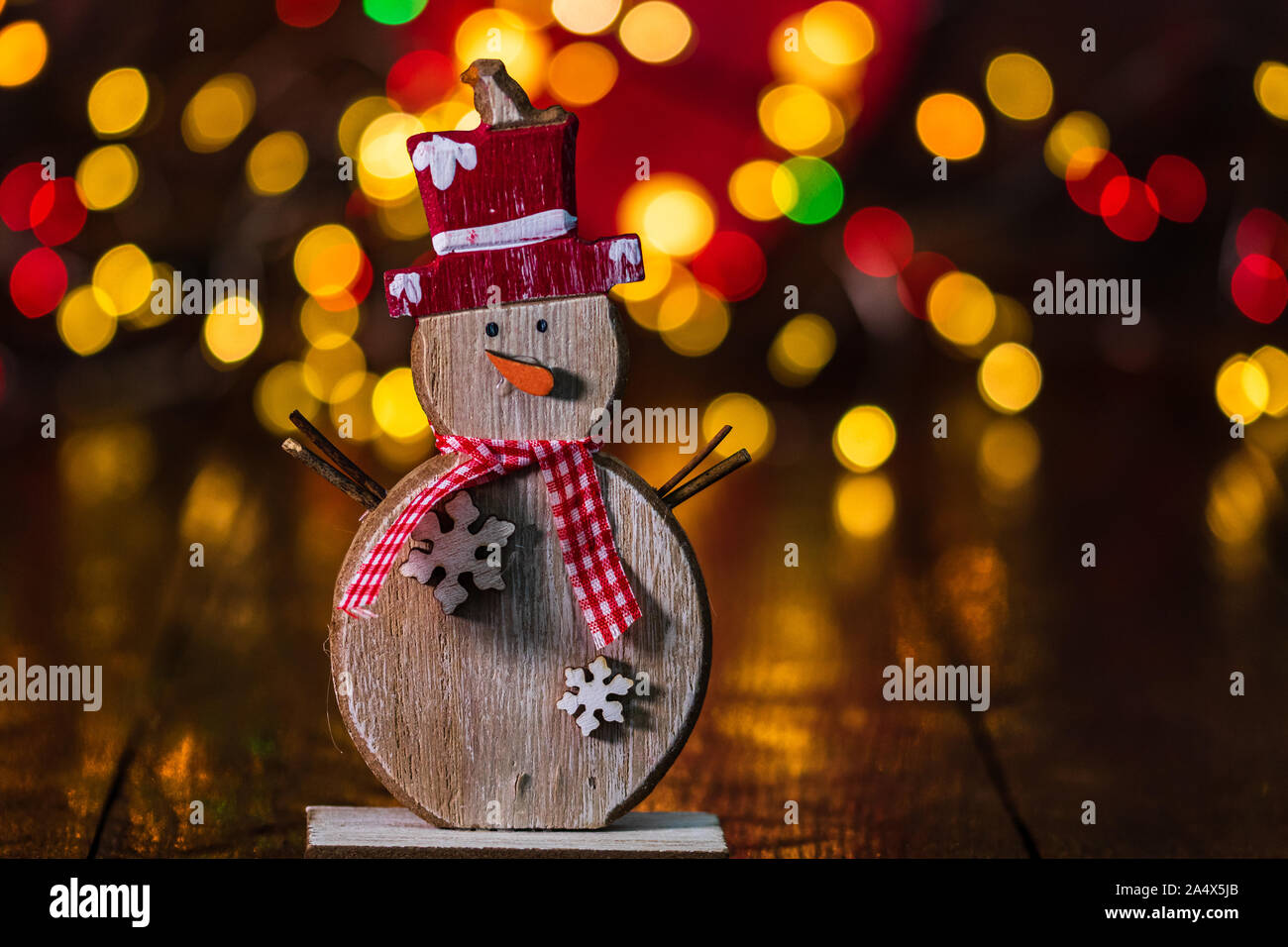 Le decorazioni di Natale contro sfondo sfocato e fuori fuoco luci. Legno decorativo pupazzo di neve e glittery palle di Natale Foto Stock
