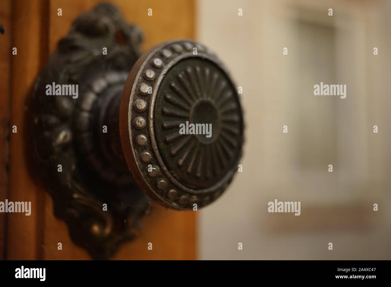 Round maniglia di ferro con un pattern su una vecchia porta di legno, primo piano. Sfondo di sfocatura di un edificio con una finestra. Foto Stock