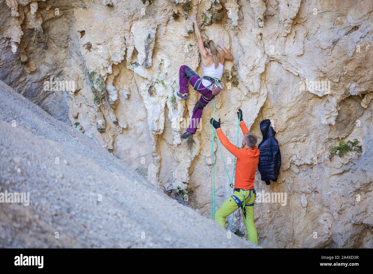 Femmina giovane scalatore a partire impegnativo percorso sulla scogliera, il suo partner belaying Foto Stock