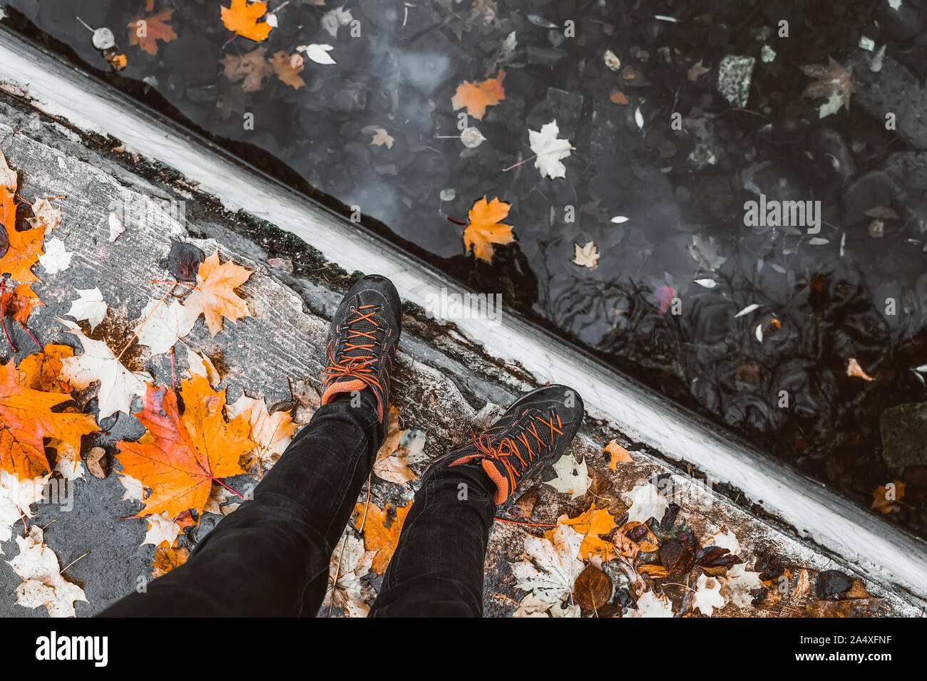 Coppia di gambe in sport sneakers accanto all'acqua, più luminose caduto foglie di autunno. Stagioni, Passeggiata d'autunno Foto Stock