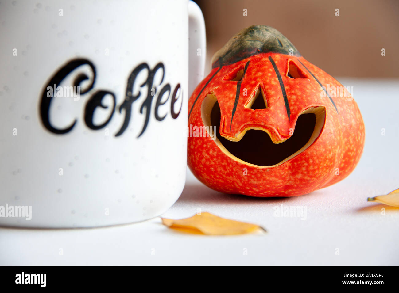 Arancione in ceramica piccolo sorriso zucca di Halloween con foglie di autunno in prossimità di essa e la tazza di caffè con il testo "caffè" su di esso. Concetto di vacanza Foto Stock