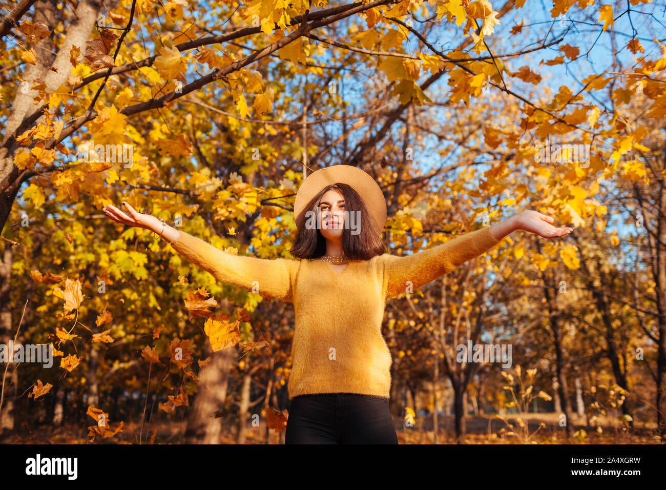 Caduta stagione attività. Donna gettando le foglie in autunno foresta al tramonto. Giovane donna avendo divertimento all'aperto indossare abbigliamento elegante Foto Stock