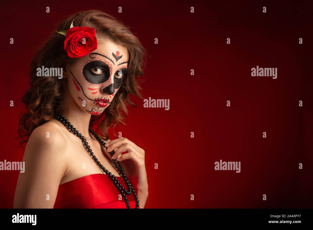 Giovane donna con santa muerte trucco su sfondo rosso con spazio copia guardando la fotocamera Foto Stock