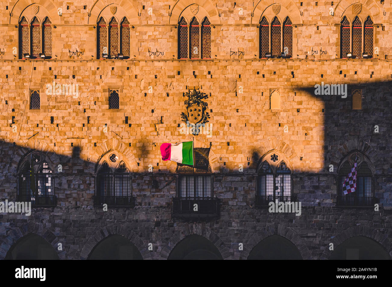 La bella facciata frontale di Pistoia medievale palazzo in pietra in Piazza Duomo di notte con la bandiera italiana e la famiglia Medici crest Foto Stock