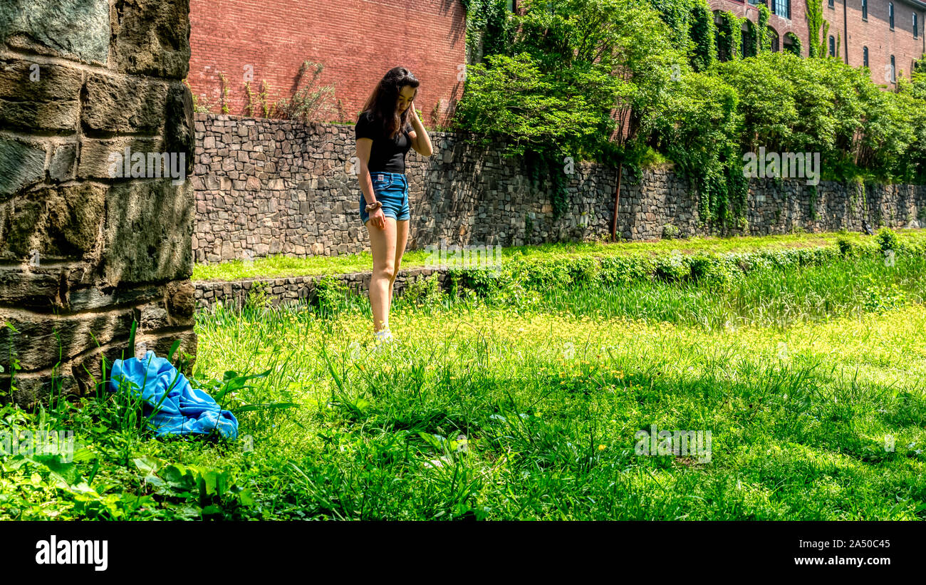 Teen girl in piedi in erba con pantaloncini blu e nero camicetta guardando in giù accanto a Chesapeake e Ohio Canal Foto Stock