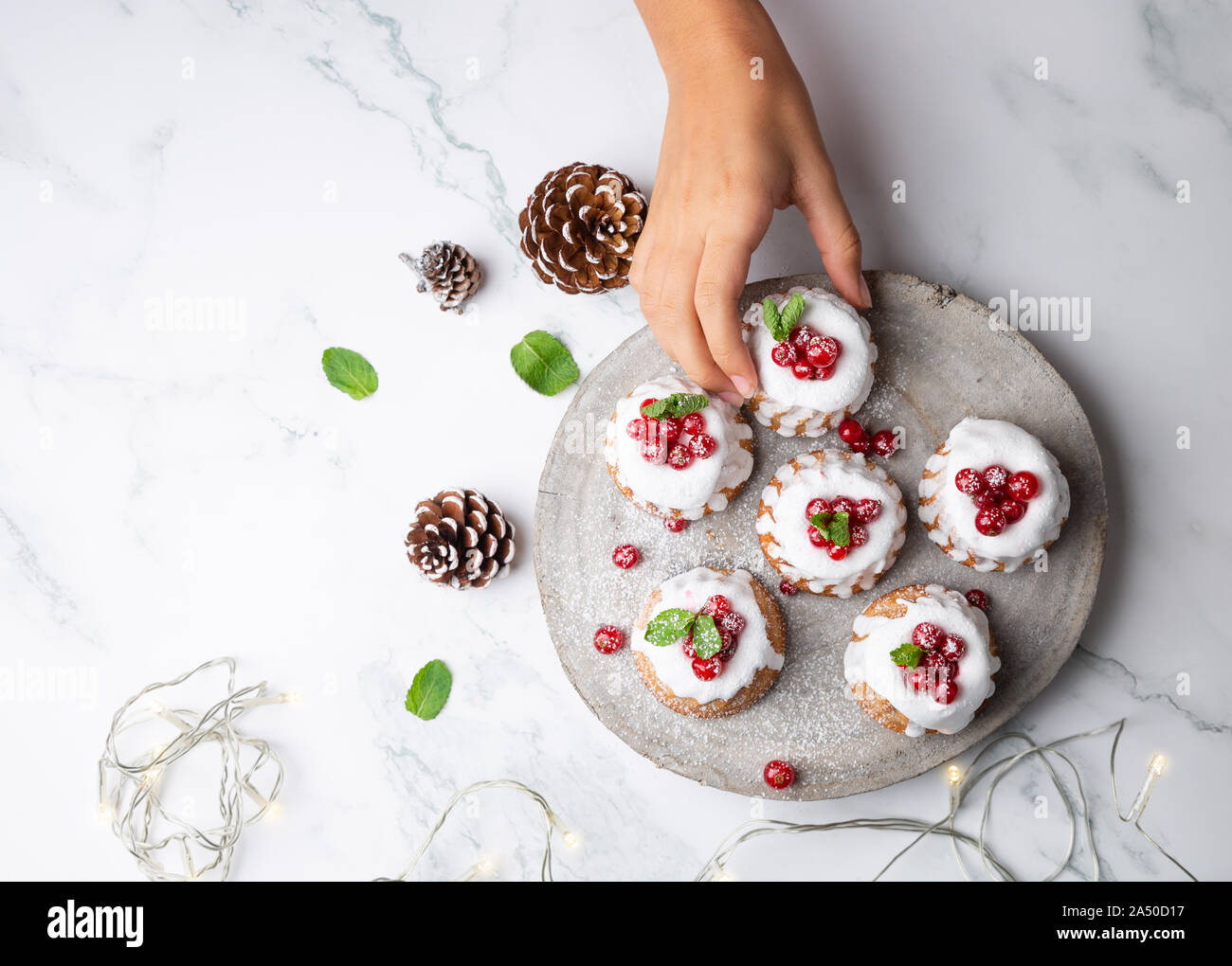 Donna raccolta a mano piccole bundt di Natale torte con glassa di zucchero e di uve secche di Corinto su di un legno rustico slice. Vista superiore Foto Stock