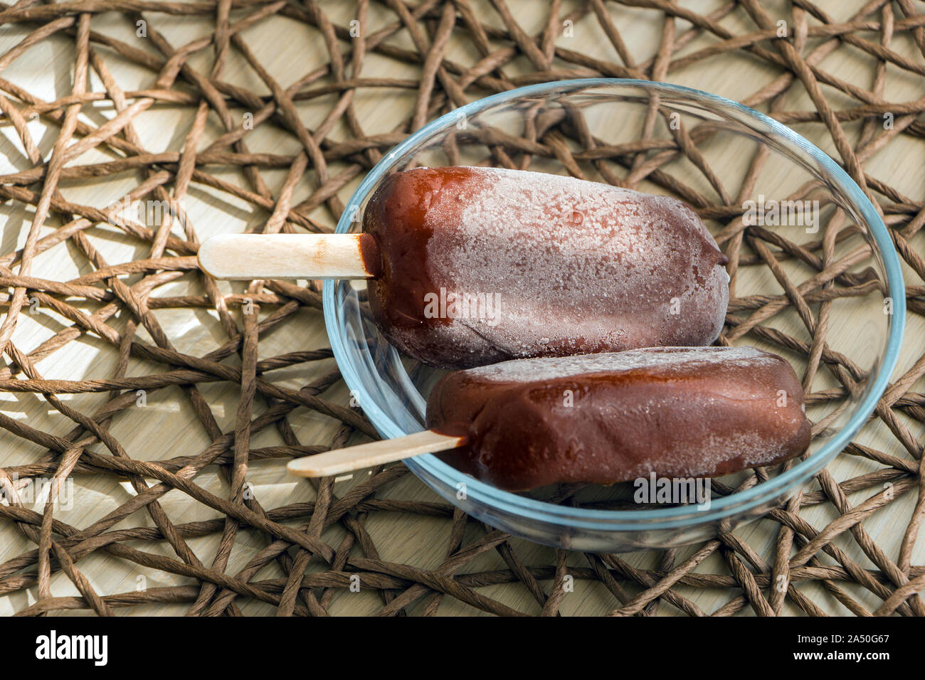 Vegano freschi cibi crudi gelato, appena estratto dal congelatore con brina su di una superficie di cioccolato. Ciotola di vetro su un tavolo con la tovaglia in vimini Foto Stock