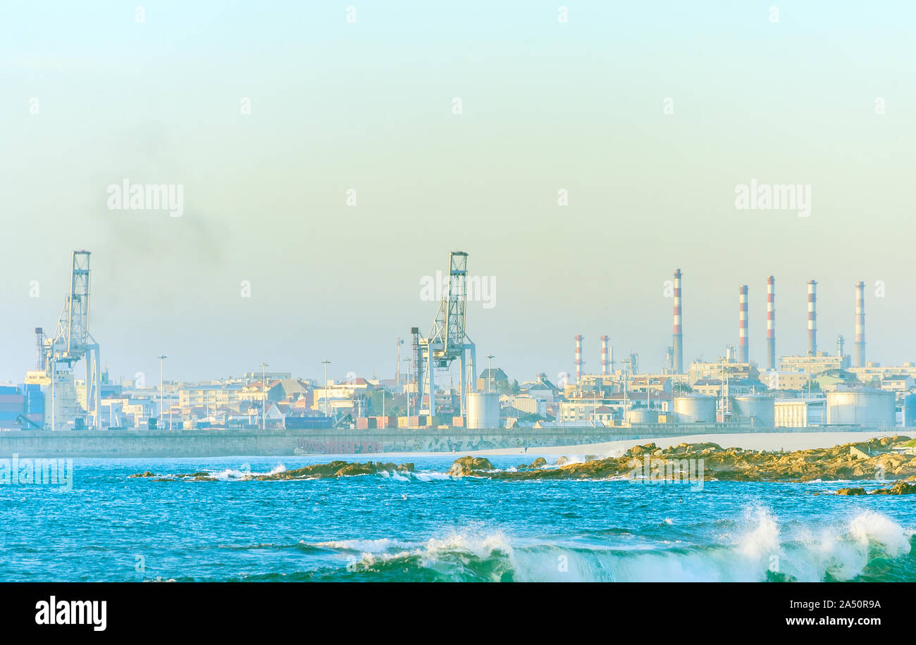 Stabilimento industriale sulla riva del mare, attrezzature portuali, nolo gru, onde brеaking on shore in presenza di luce solare, Porto, Portogallo Foto Stock