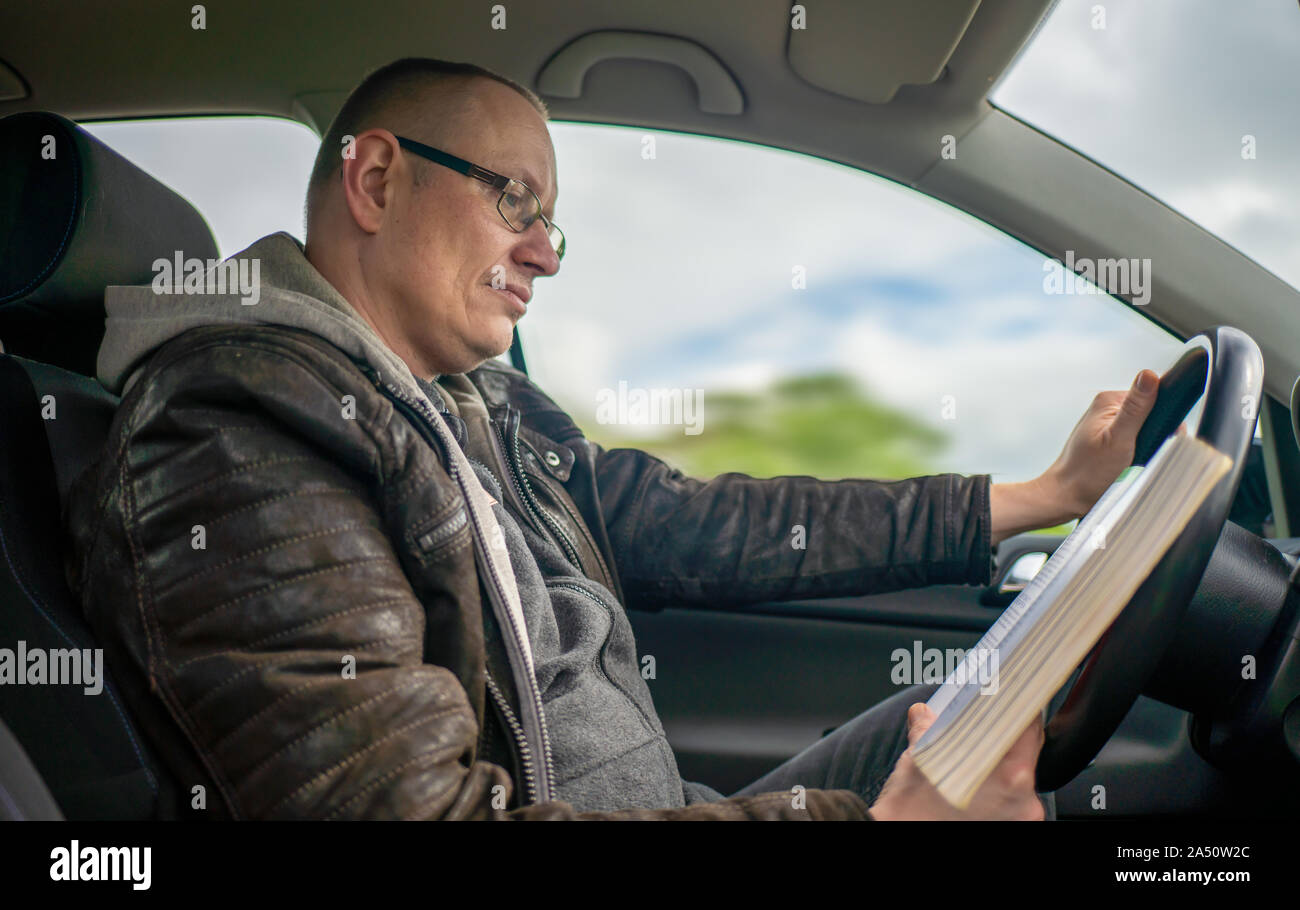 Un uomo è la lettura di un libro mentre sei alla guida di una vettura ed è distratto Foto Stock