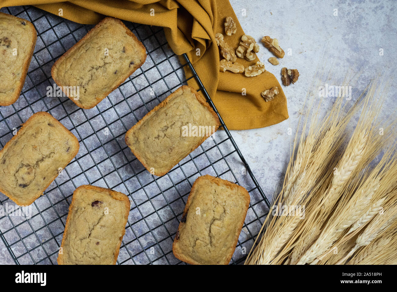 Mini pirottini di pani su un filo nero rack di cottura con un tovagliolo oro, noci e covoni di grano su un bancone di marmo Foto Stock