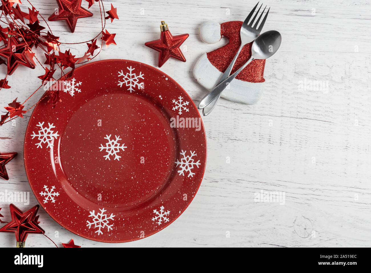 Festosa vacanza invernale luogo impostazione con i fiocchi di neve sulla targhetta rossa, star decor e santa hat con cucchiaio e forchetta su un rustico verniciato bianco backgro legno Foto Stock