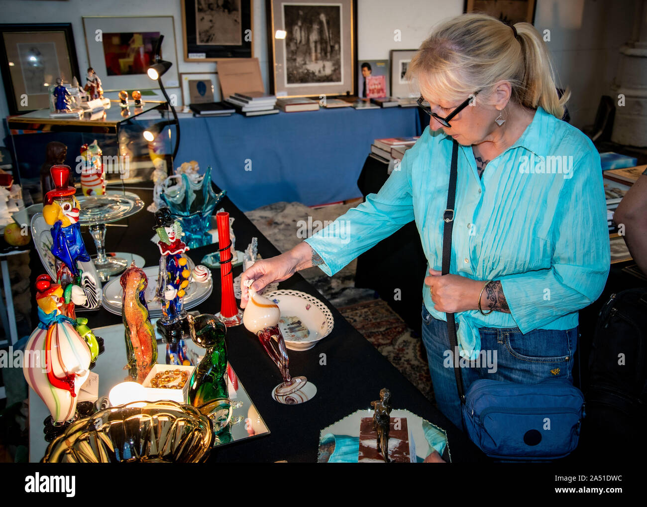 donna di mezza età alla ricerca di occasioni alla fiera dell'artigianato e dell'antiquariato, mostrando particolare interesse al clown di vetro, stalla, Foto Stock