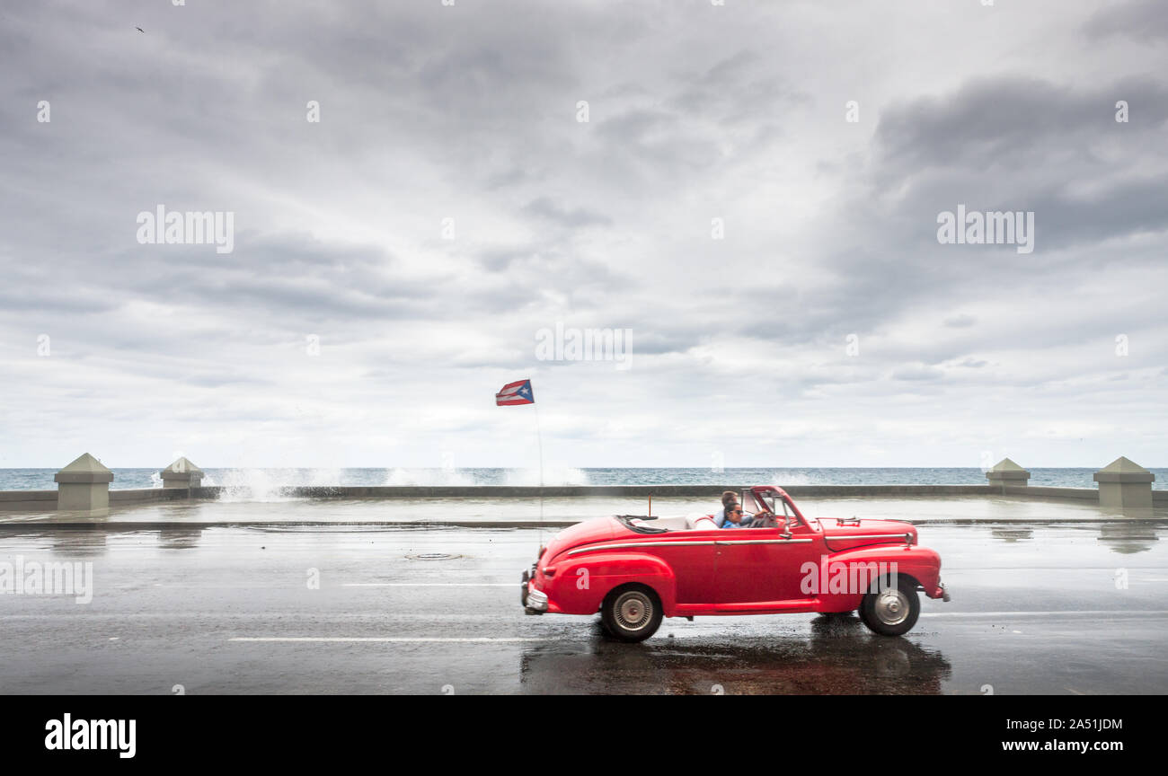 L'Avana, Cuba. 18 gennaio, 2013. Un vecchio American automobile convertibile aziona verso il basso il Malecón su una giornata di gennaio come onde giro oltre la parete del mare in ha Foto Stock