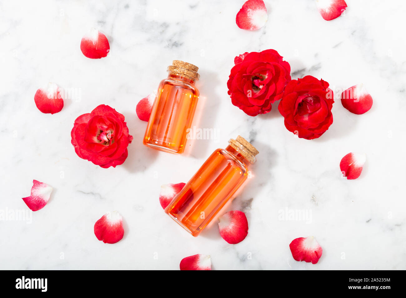 Rose profumate di acqua in bottiglia di vetro e piccole rose rosse con petali . Massaggi, aromaterapia e cosmetici biologici concept Foto Stock