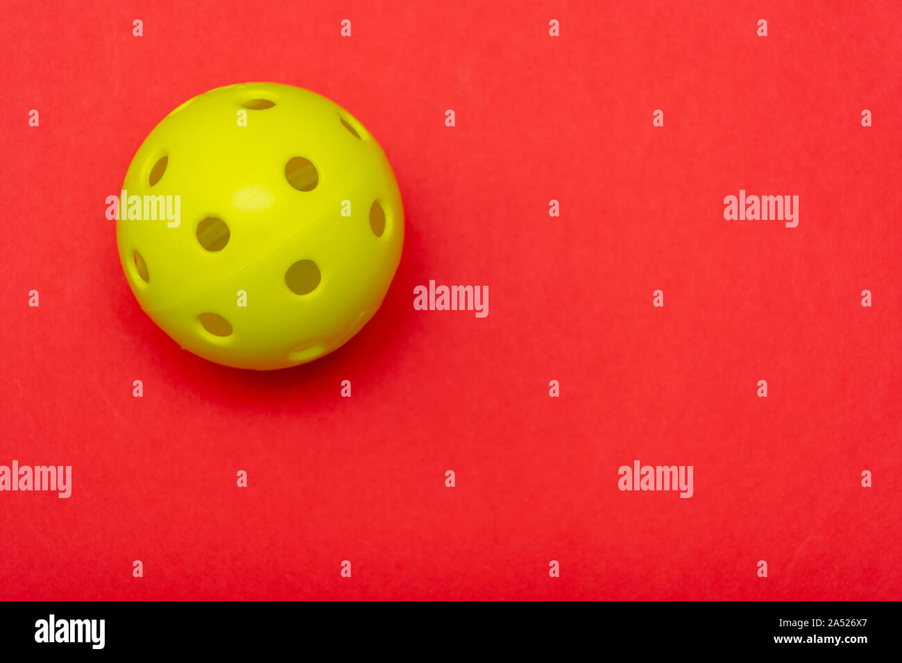 Di colore giallo brillante pickleball o sfera whiffle su un solido rosso luminoso appartamento sfondo laici che simboleggiano sport e attività con copia spazio. Foto Stock