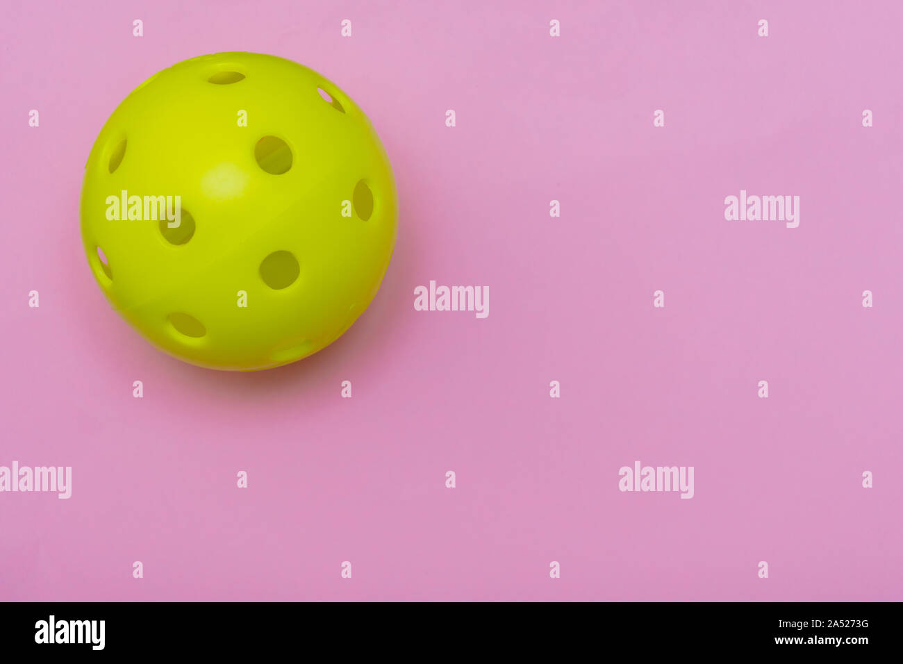 Di colore giallo brillante pickleball o sfera whiffle su un solido rosa luminoso appartamento sfondo laici che simboleggiano sport e attività con copia spazio. Foto Stock