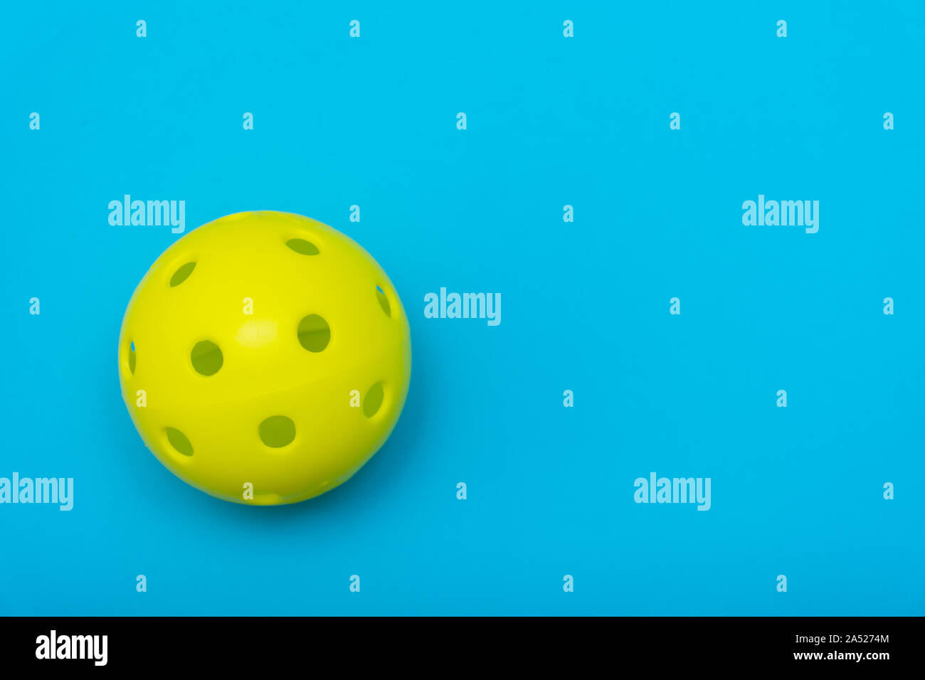 Di colore giallo brillante pickleball o sfera whiffle su un solido aqua blue piatto sfondo laici che simboleggiano sport e attività con copia spazio. Foto Stock