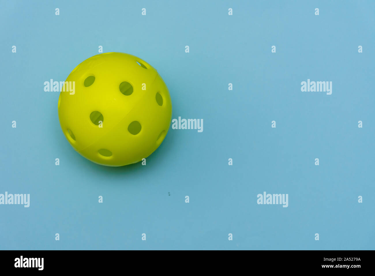 Di colore giallo brillante pickleball o sfera whiffle su un solido aqua blue piatto sfondo laici che simboleggiano sport e attività con copia spazio. Foto Stock