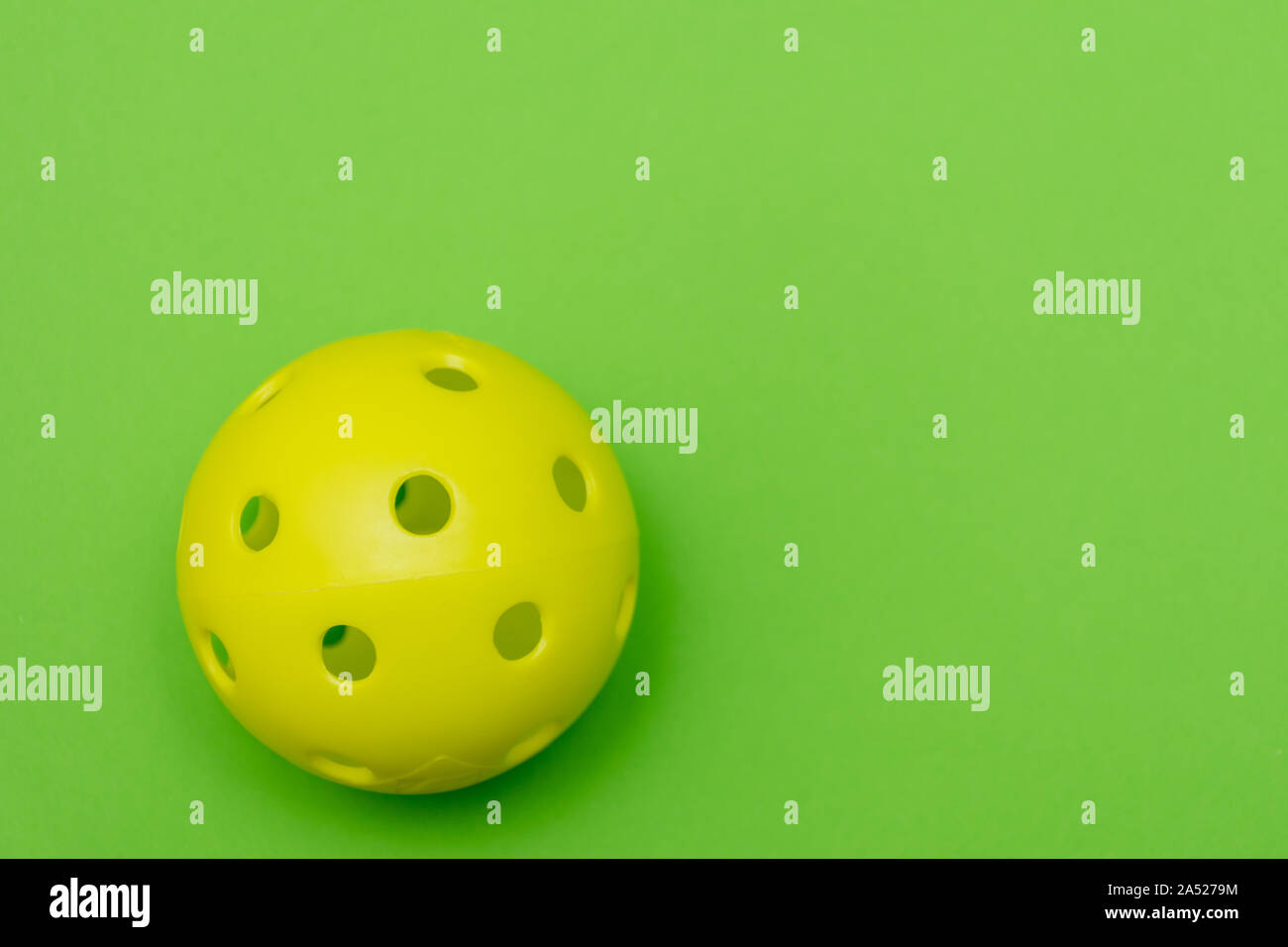 Di colore giallo brillante pickleball o sfera whiffle su un solido verde chiaro piatto sfondo laici che simboleggiano sport e attività con copia spazio. Foto Stock