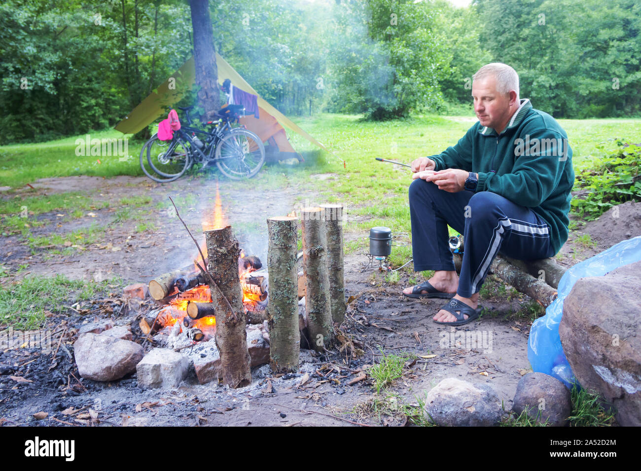 Un uomo arrosti salsicce su un falò, tenda bici e falò, la regione di Kaliningrad, Russia, 1 Agosto 2019 Foto Stock