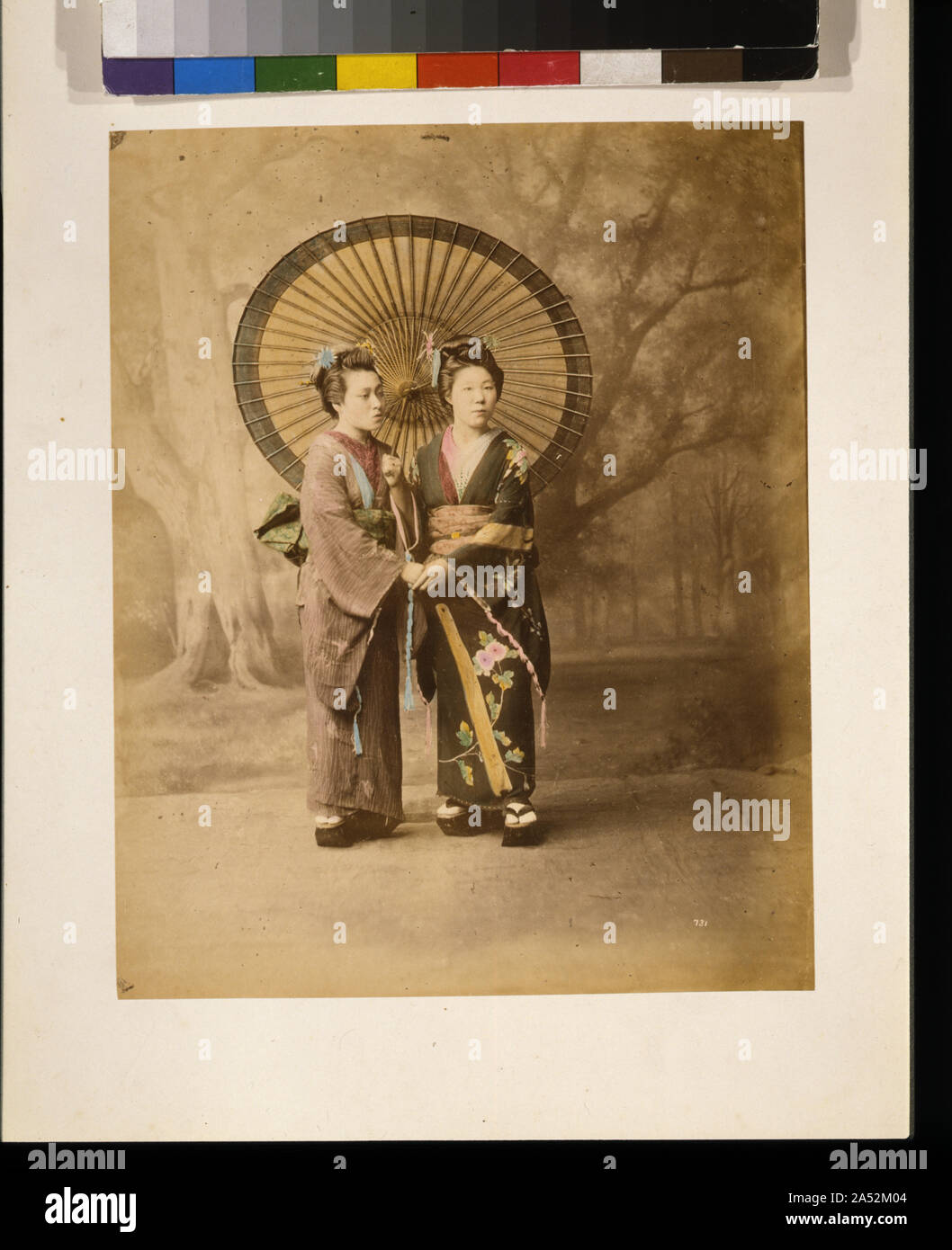 Due donne giapponesi e a piena lunghezza ritratto in studio con sfondo, rivolta leggermente a destra, in piedi con ombrellone e tenendo le mani Foto Stock