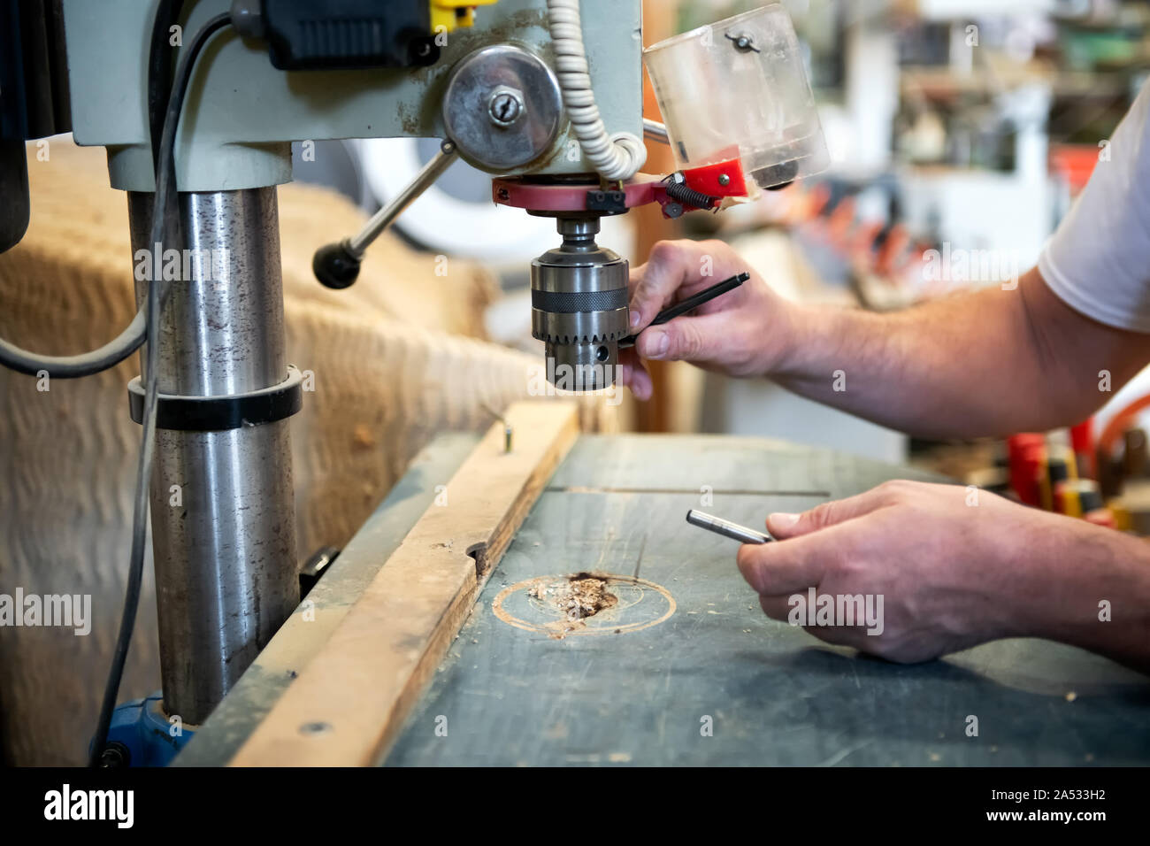 Carpenter cambiando il bit su un trapano verticale in un laboratorio di falegnameria in un vicino fino alle mani Foto Stock