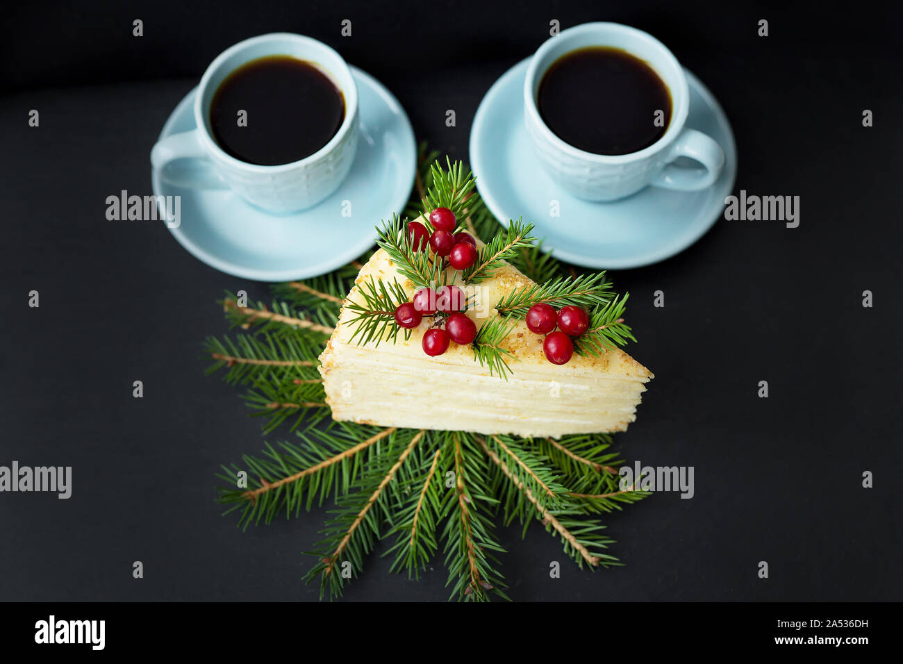 Pezzo di torta decorata ad albero e frutti di bosco su un fondo nero con due tazze di caffè. Foto Stock