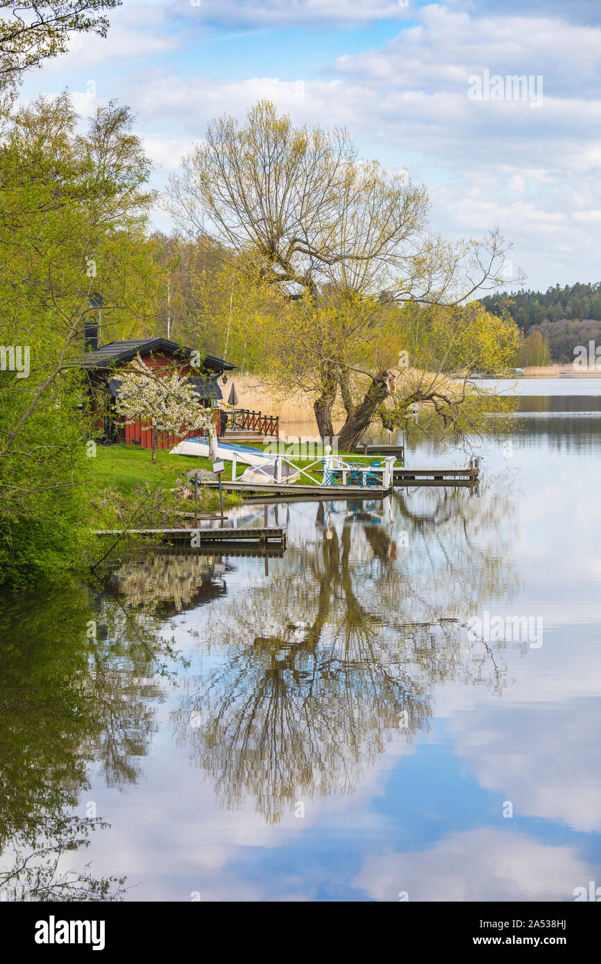 Primavera prendere vista con un piccolo cottage di rosso e gli alberi con riflessi nell'acqua. Foto Stock