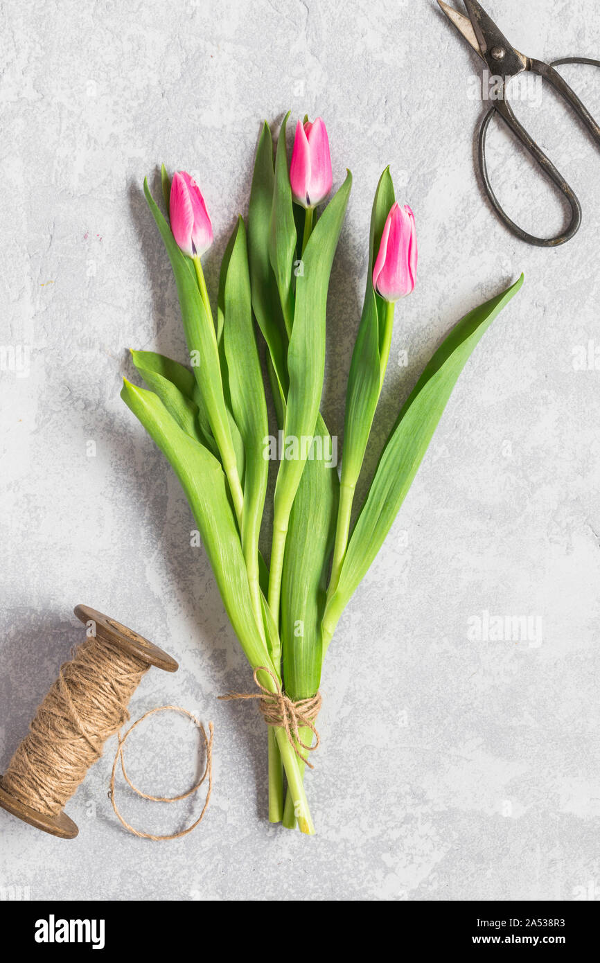 Un semplice bouquet di tulipani su sfondo grigio, visto da sopra.I tre tulipani sono rosa e sono legati insieme da una corda di iuta. Vi è una bobina e un p Foto Stock