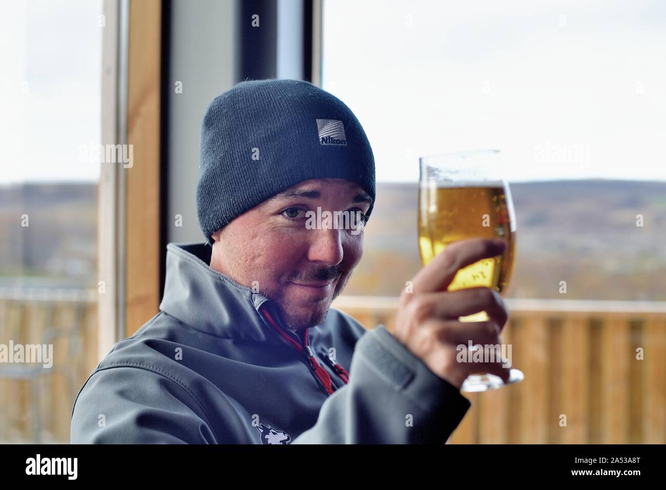 Reykholt, Islanda. Un turista avente una birra durante la pausa per il pranzo in un ristorante al di sopra delle cascate Hraunfosser vicino a Reykholt.winter hat Foto Stock